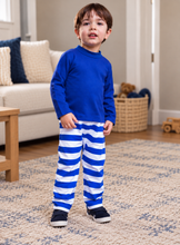A young boy wearing a royal blue long-sleeve shirt and blue and white striped pants, standing on a patterned rug in a living room setting.