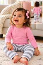 A toddler girl sitting on a cream carpet in a living room, wearing a pink long-sleeve top with a pink zipper back and gray-and-white striped pants. An inset in the top right shows the back view of the outfit.