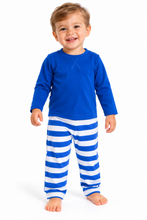 A smiling toddler standing against a white studio background, wearing a bright blue long-sleeve top and matching blue-and-white horizontally striped pants.