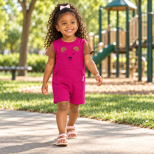 A young girl with curly hair walking on a paved path in a sunny park, wearing a bright pink sleeveless romper with brown sleeves and a bear face graphic.