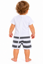 A baby viewed from the back wearing a white short-sleeve romper with a full-length zipper and dark gray and white horizontal striped shorts, standing against a plain white background.