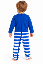 A toddler standing with their back to the camera, wearing a blue and white striped footed sleeper with a full-length zipper.