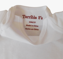 Close-up of the inside collar of a white baby or toddler t-shirt, showing the printed red brand label 'Terrible 2's' along with size and origin text.