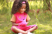 Toddler girl in pink and brown strip free romper sitting on grass 